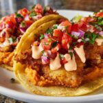 Two freshly made fish tacos with crispy fish, salsa, and a creamy sauce, perfect for Taco Tuesday.