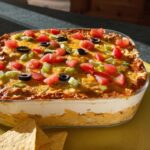 A delicious layered taco dip with tomatoes, olives, and cheese, perfect for Taco Tuesday recipes.