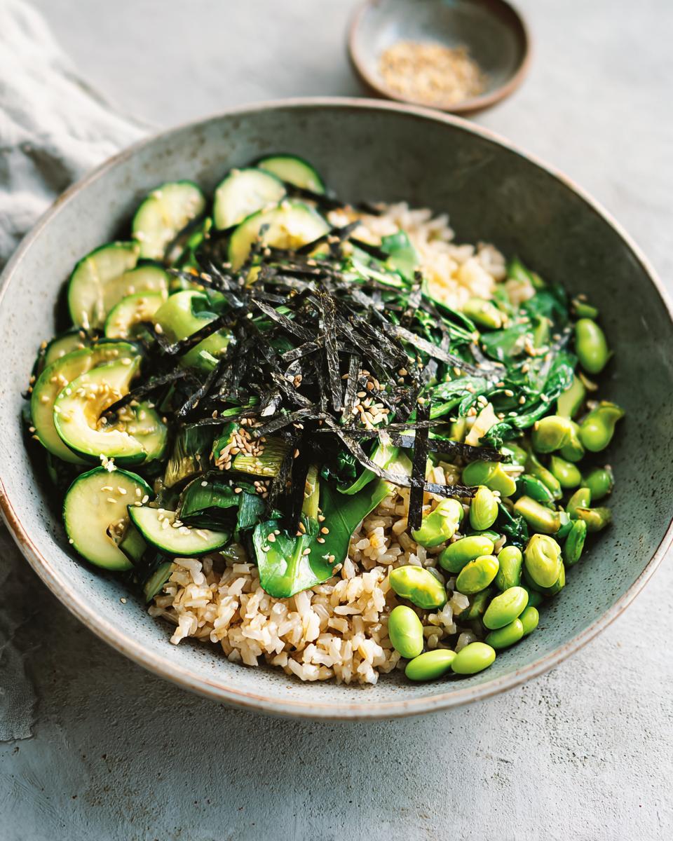 A vibrant and healthy vegetarian rice bowl filled with brown rice, edamame, zucchini, greens, and nori.