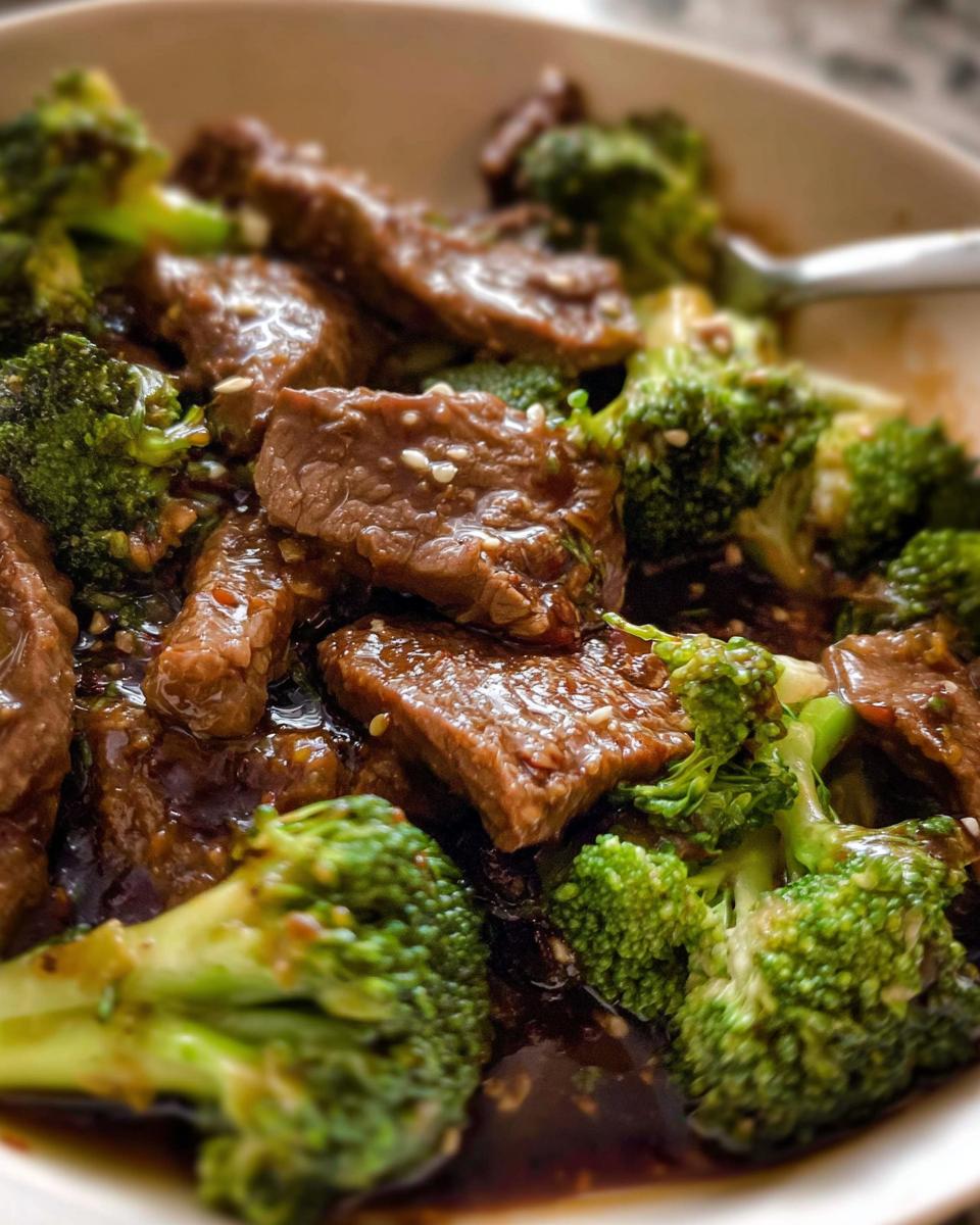 Close-up of tender slices of Chinese Beef and Broccoli coated in a savory sauce, sprinkled with sesame seeds.