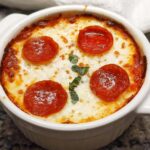 A close-up of a baked Cottage Cheese Pizza Bowl topped with melted cheese, pepperoni slices, and fresh basil.