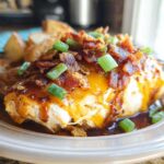 A juicy piece of Cowboy BBQ Bacon Cheddar Chicken topped with melted cheddar cheese, crispy bacon, and green onions, served with roasted potatoes.