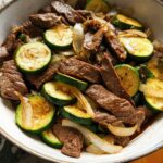 A close-up of a Cozy Grilled Steak Bowl with Zucchini and onions, showcasing tender steak slices and vibrant zucchini rounds.