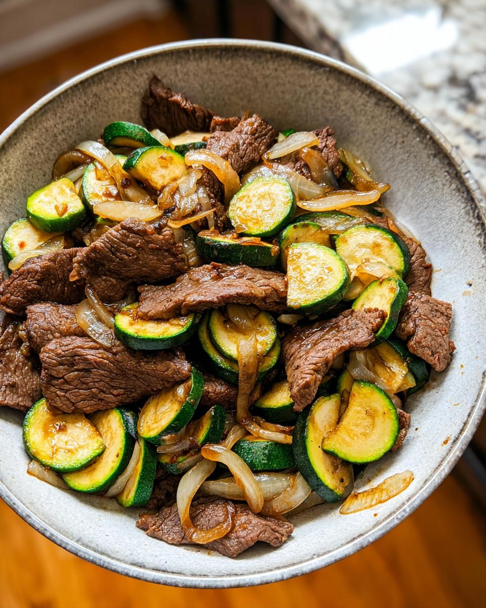A close-up of a Cozy Grilled Steak Bowl with Zucchini and onions, showcasing tender steak slices and vibrant zucchini rounds.