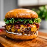 A mouthwatering Crack Burger featuring a juicy beef patty, melted cheddar cheese, crispy bacon, fresh lettuce, and creamy sauce on a toasted bun.