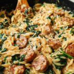 Close-up of Creamy Chicken Sausage Orzo with wilted spinach and grated cheese, a wooden spoon is visible.