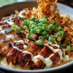 A bowl of Creamy Garlic Chicken Ramen topped with sliced grilled chicken, green onions, and a drizzle of sauce.
