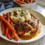 A plate of Creamy Herb Chicken with Mashed Potatoes & Glazed Carrots, drizzled with sauce and sprinkled with parsley.