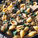 A close-up of Creamy High Protein Beef Pasta with spinach, served in a cast-iron skillet with a wooden spoon.