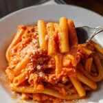 A fork lifting a portion of creamy tomato garlic pasta, showing the rich sauce coating the rigatoni.