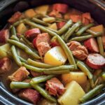 Close-up of Crockpot Kielbasa and Green Beans cooking in a black slow cooker, showing potatoes, sausage slices, and green beans in broth.