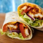 Two halves of Crunchy Crispy Air Fryer Chicken & Mozzarella Wraps filled with lettuce, tomato, red onion, and melted cheese.