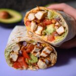 A halved Easy Chipotle Ranch Grilled Chicken Burrito showing grilled chicken, avocado, tomatoes, lettuce, and red onion.