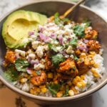 A delicious Easy Street Corn Chicken Bowl topped with avocado, crumbled cheese, red onion, and cilantro.