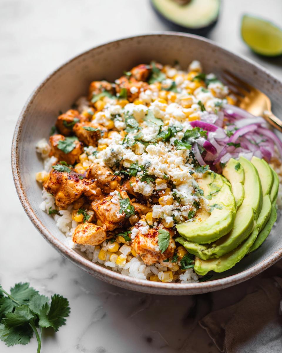 A close-up of an Easy Street Corn Chicken Bowl featuring rice, seasoned chicken, corn, crumbled feta, sliced avocado, and red onion.