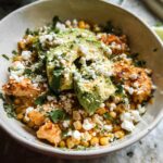 A close-up of an Easy Street Corn Chicken Bowl topped with sliced avocado, crumbled cheese, and fresh cilantro.