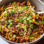 A close-up of a bowl filled with Egg Roll in a Bowl, featuring ground meat, cabbage, and green onions, topped with sesame seeds.