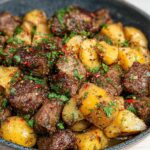 Close-up of Garlic Steak Bites and Potatoes, seasoned with herbs and chili flakes, served in a dark bowl.