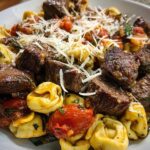 A close-up of Garlic Steak Tortellini, featuring tender steak bites, golden tortellini, and roasted tomatoes, topped with shredded cheese.