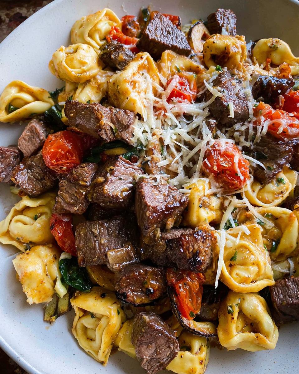 Close-up of a bowl of Garlic Steak Tortellini with tender steak pieces, tortellini pasta, cherry tomatoes, and shredded cheese.