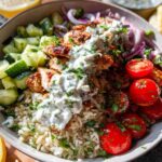 A close-up of a vibrant Greek Chicken Bowl, featuring seasoned chicken, rice, cucumber, tomatoes, red onion, and tzatziki sauce.