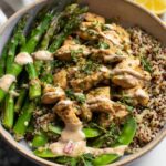 A healthy lemon garlic chicken meal prep bowl filled with quinoa, asparagus, and snow peas, drizzled with sauce.