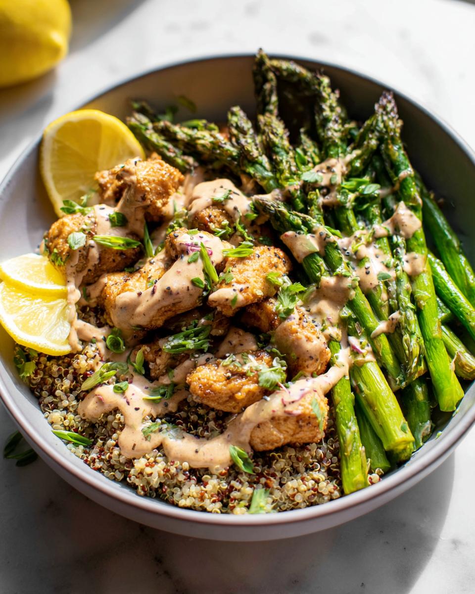 A healthy lemon garlic chicken meal prep bowl with quinoa, asparagus, and a creamy sauce.