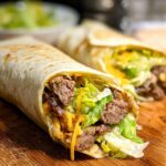 Two delicious Homemade Big Mac Wraps filled with seasoned beef, shredded lettuce, and melted cheese on a wooden board.