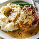 A plate of Irresistible Garlic Herb Chicken served with creamy mashed potatoes and green beans, drizzled with sauce.