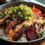 A close-up of Korean BBQ Steak Rice Bowls topped with spicy cream sauce, scallions, and sesame seeds.