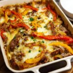 A baked Low Carb Philly Cheesesteak Casserole in a white baking dish, topped with melted cheese and bell peppers.