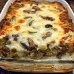 A baked Low Carb Philly Cheesesteak Casserole in a white dish, topped with melted cheese, peppers, and mushrooms.