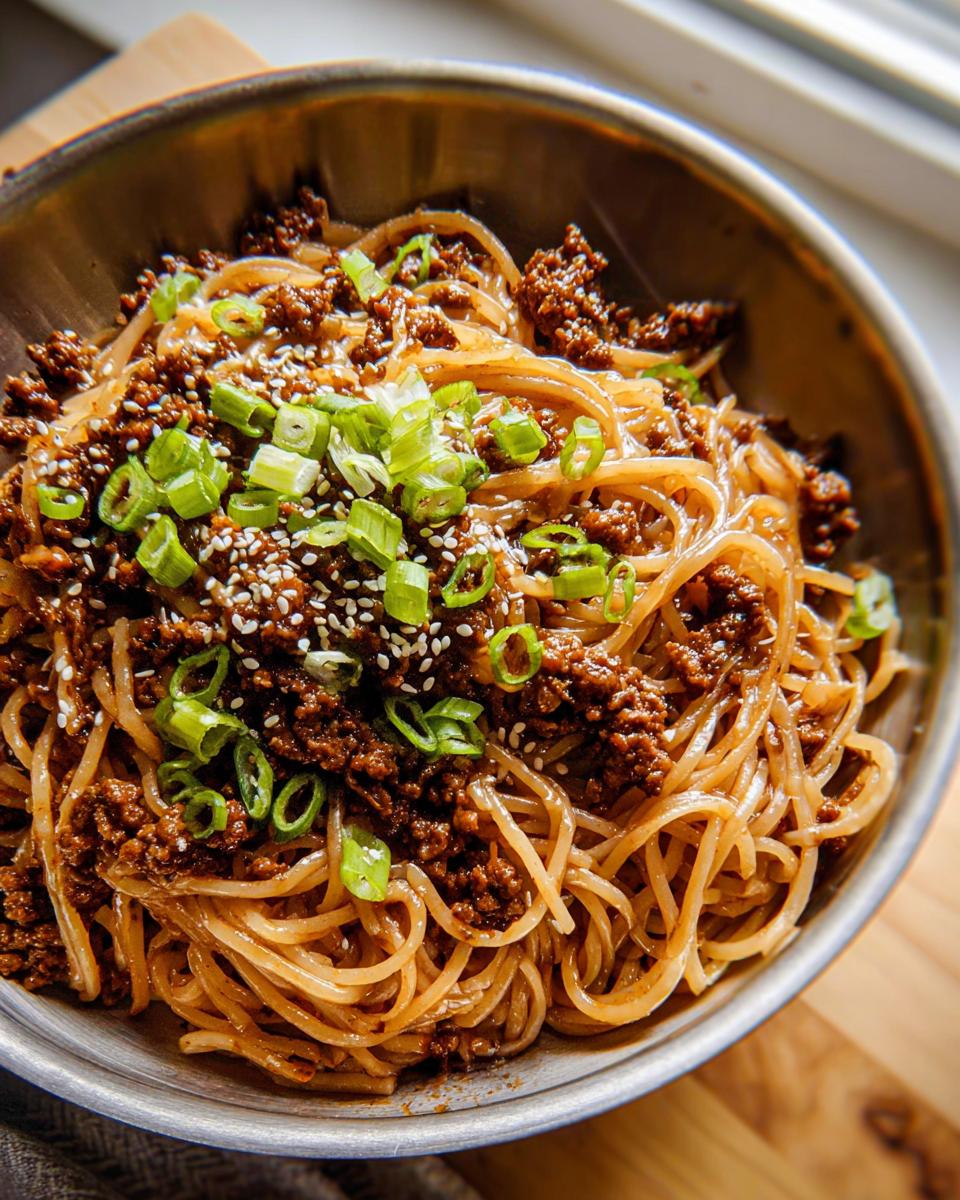 A close-up of Mongolian Ground Beef Noodles in a bowl, topped with sesame seeds and green onions.