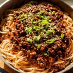 A close-up of Mongolian Ground Beef Noodles, topped with sesame seeds and green onions.