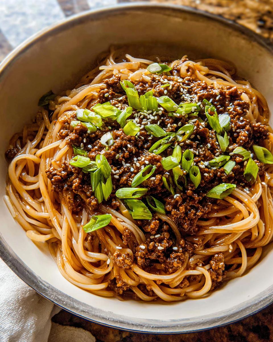 A close-up bowl of Mongolian Ground Beef Noodles, topped with green onions and sesame seeds.