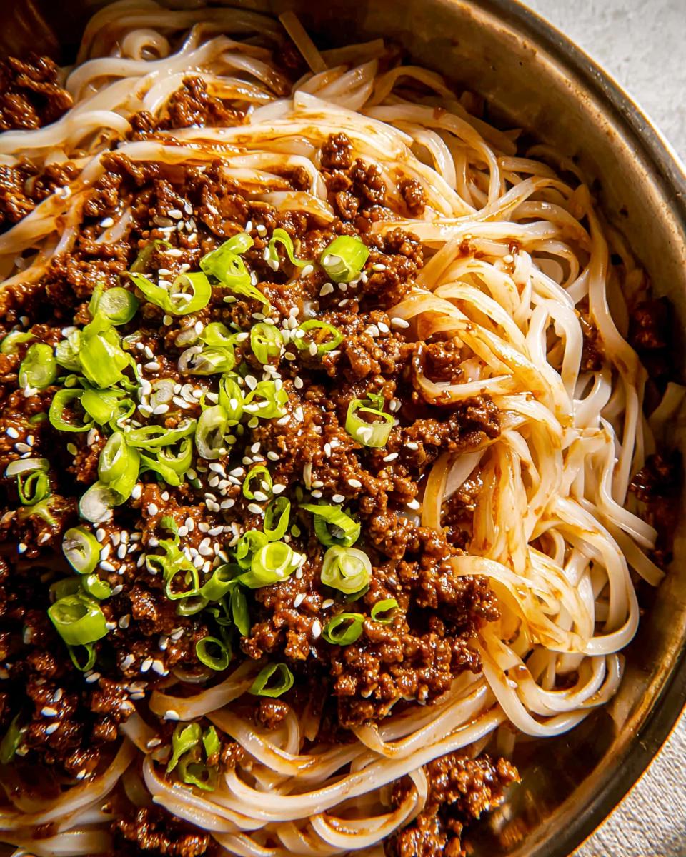 A close-up of Mongolian Ground Beef Noodles, featuring savory ground beef, white noodles, and green onions, topped with sesame seeds.