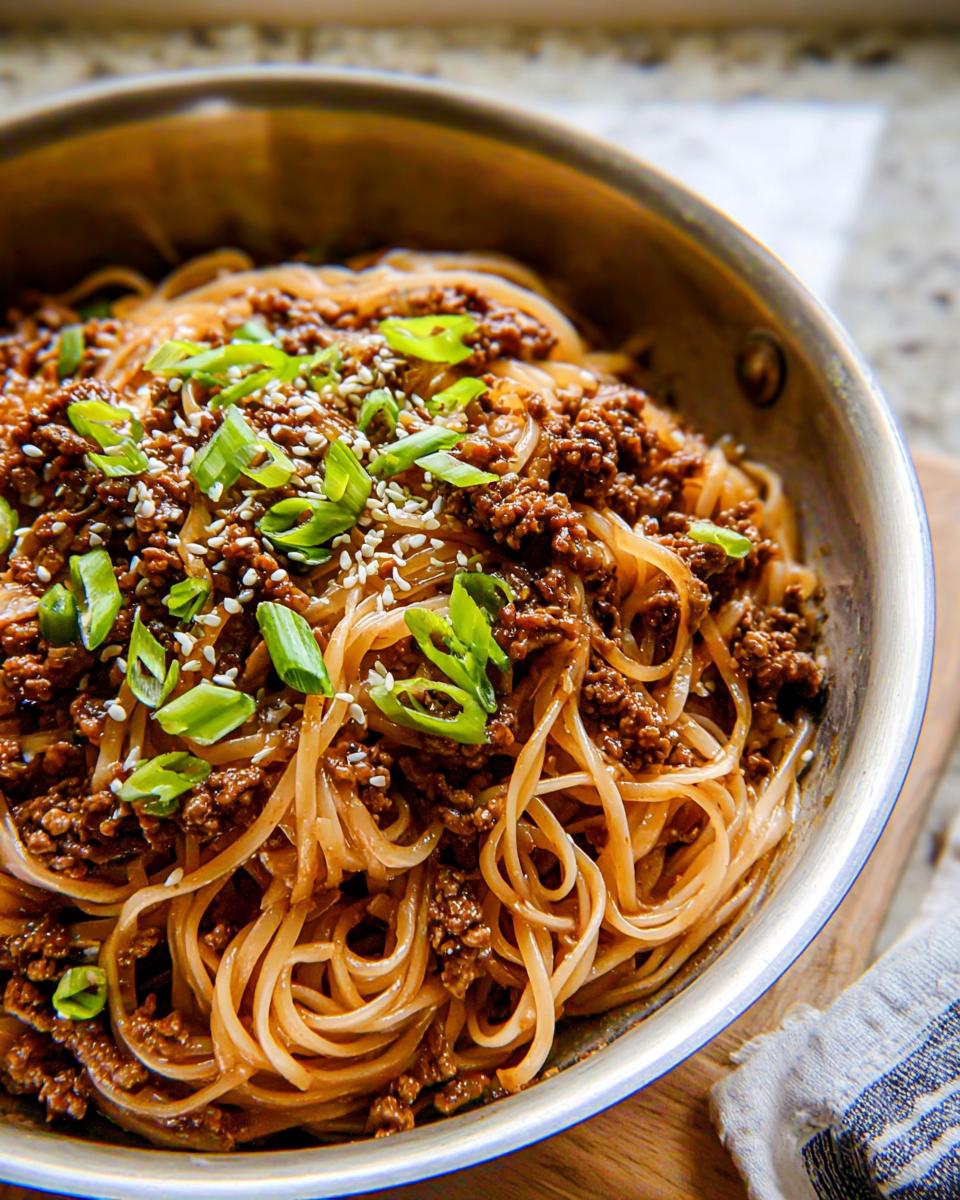 A close-up shot of Mongolian Ground Beef Noodles, garnished with sesame seeds and chopped green onions.