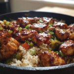 A close-up of a one-pan honey BBQ chicken rice dish, featuring glazed chicken pieces nestled in rice with vegetables.
