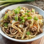 A close-up of a bowl filled with a delicious Potsticker Noodle Bowl featuring pork, noodles, cabbage, and green onions.