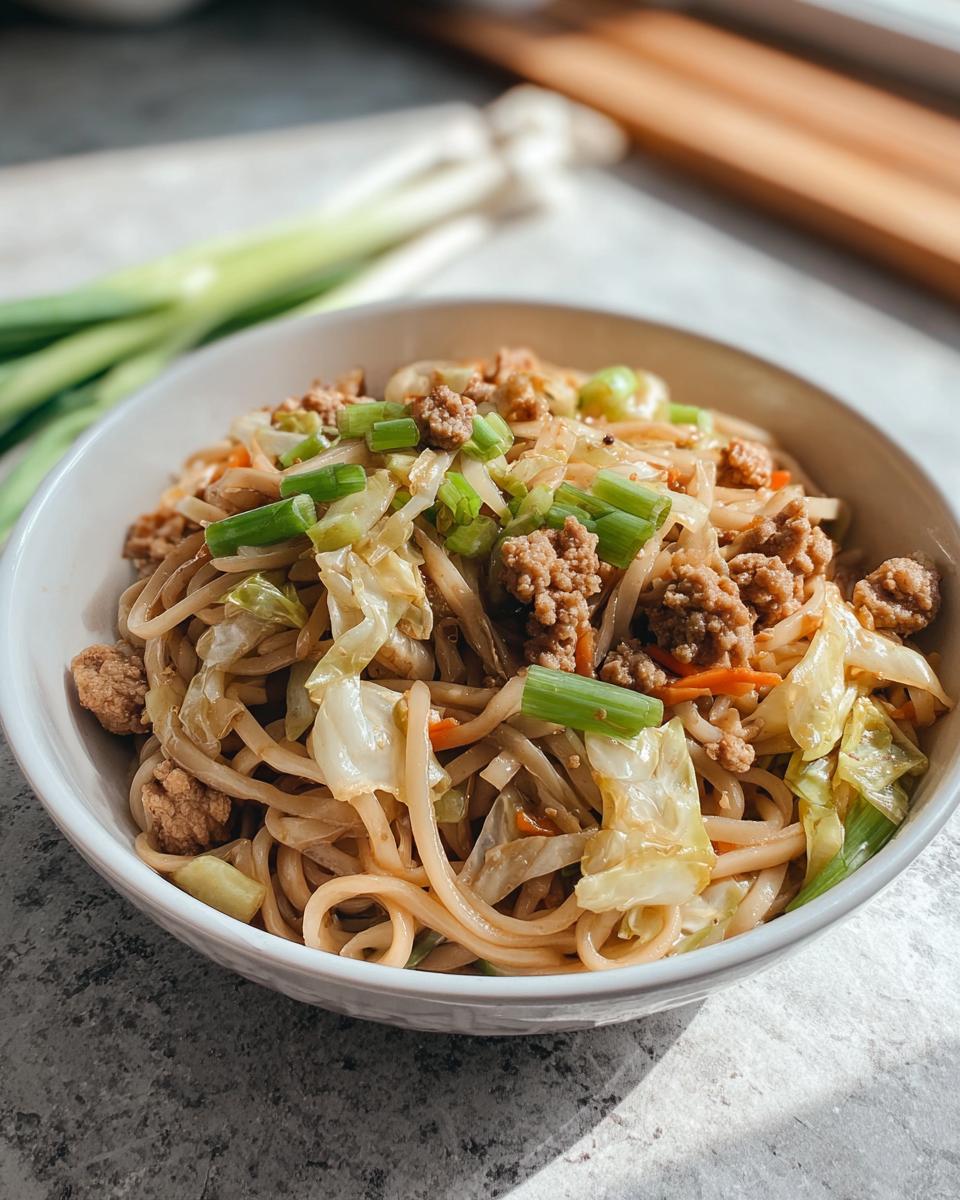 A close-up of a Potsticker Noodle Bowl with Pork & Cabbage, featuring noodles, ground pork, cabbage, and green onions.