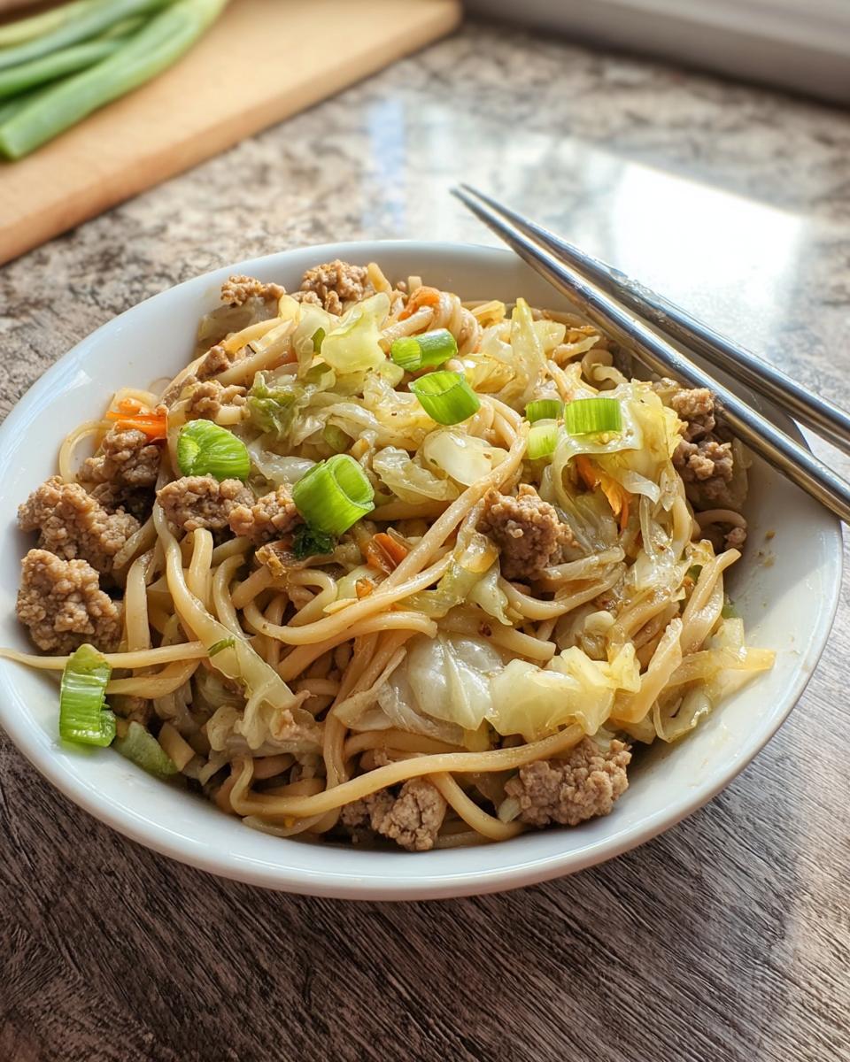 A close-up of a white bowl filled with a Potsticker Noodle Bowl with Pork & Cabbage Slaw, topped with green onions.
