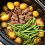 Overhead view of slow cooker garlic butter beef with potatoes and green beans.