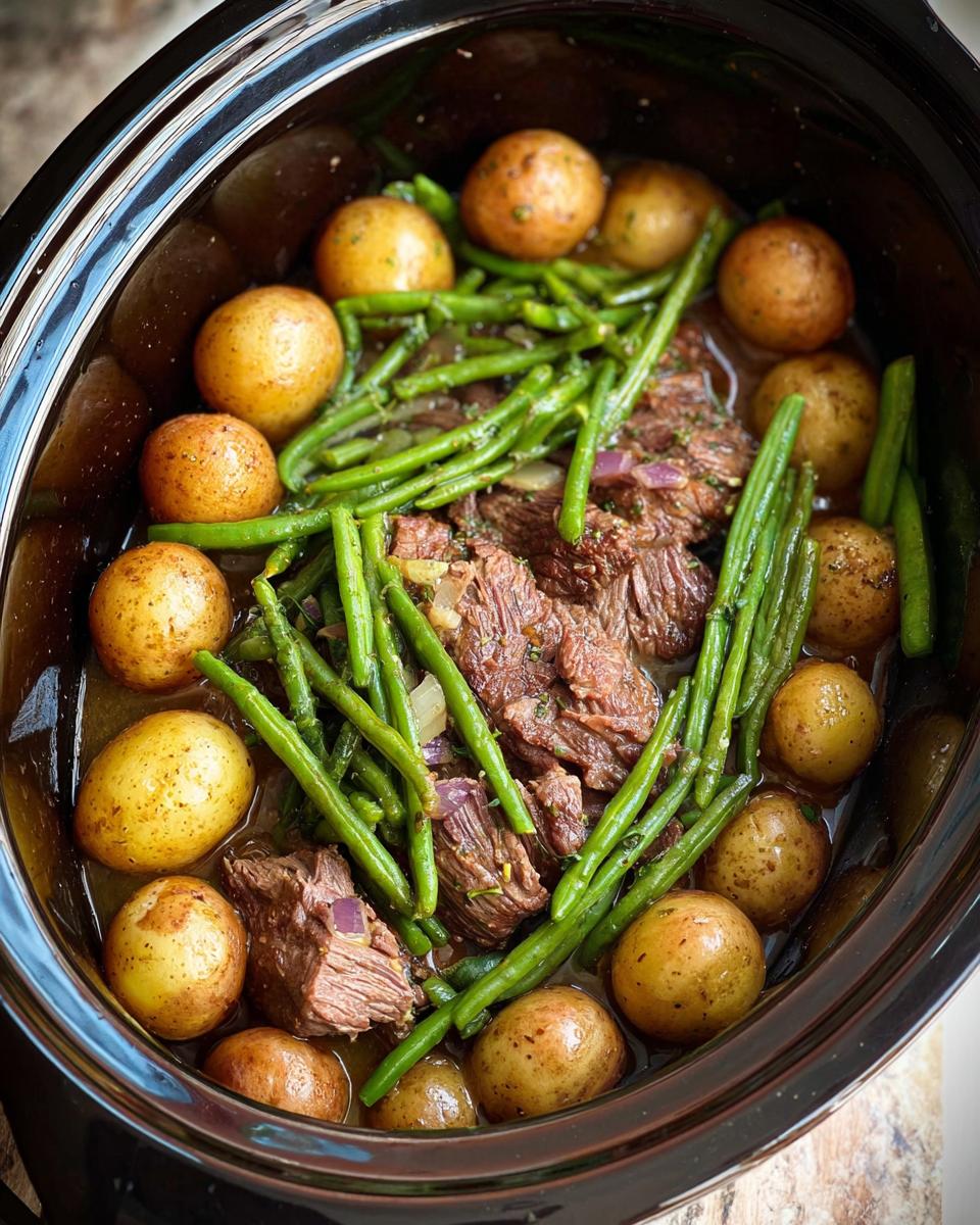 Overhead view of Slow Cooker Garlic Butter Beef with Potatoes and Green Beans in a black crock pot.