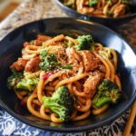 A close-up of a bowl of Spicy Garlic Chicken and Broccoli Noodle Bowls, featuring udon noodles, chicken, and broccoli.