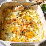 Close-up of baked feta eggs in a baking dish, with runny yolks and fresh herbs.