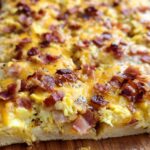 Close-up of a slice of breakfast pizza with scrambled eggs, melted cheese, and crispy bacon.