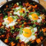 A hearty BREAKFAST SWEET POTATO skillet with fried eggs, crispy bacon, kale, and green onions.