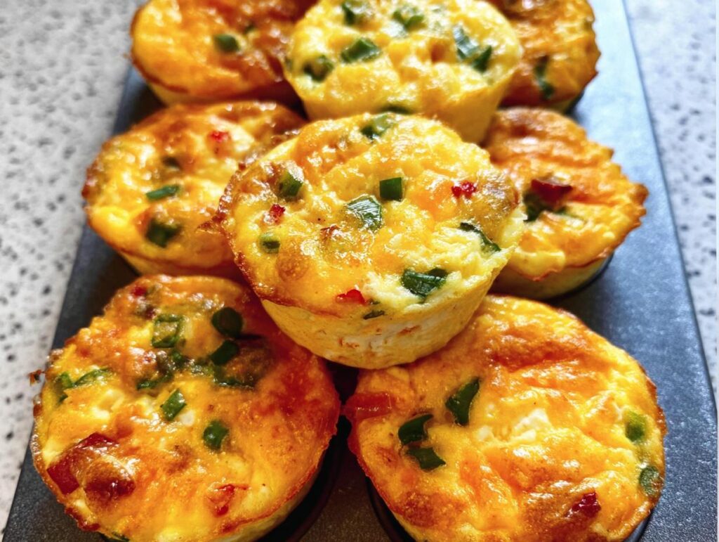 A close-up of several golden-brown Cheesy Muffin Tin Cottage Cheese Egg Bites with visible green onions and red peppers.
