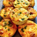 A close-up of several golden-brown Cheesy Muffin Tin Cottage Cheese Egg Bites with visible green onions and red peppers.