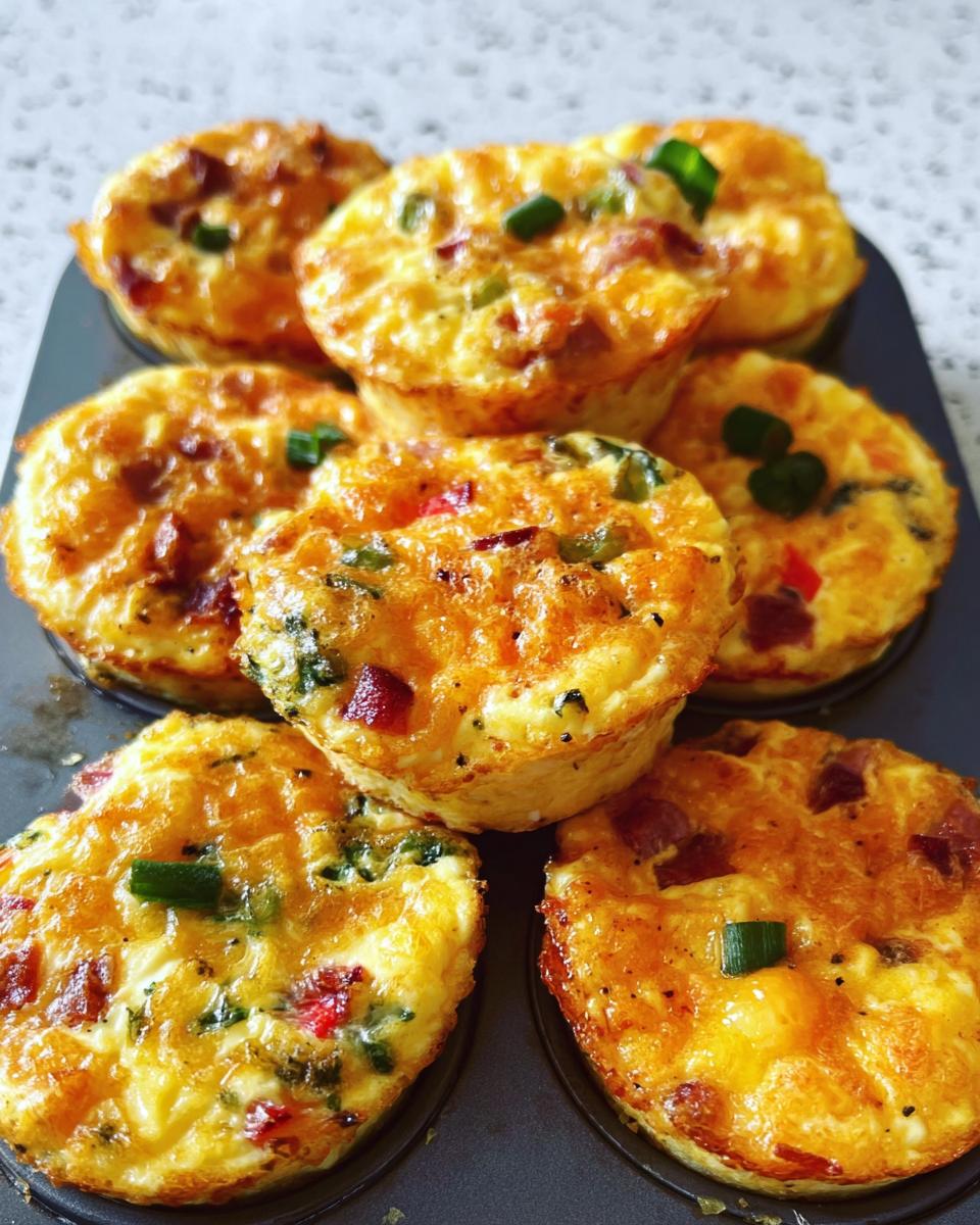 A close-up of cheesy muffin tin cottage cheese egg bites with visible pieces of bacon, peppers, and green onions.
